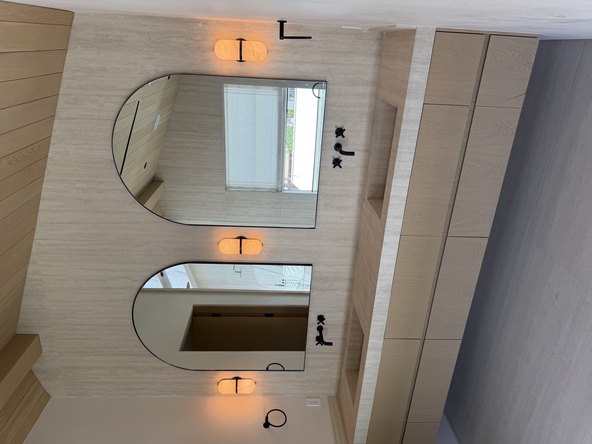 Two arched custom mirrors installed above a double stone vanity with matte black fixtures
