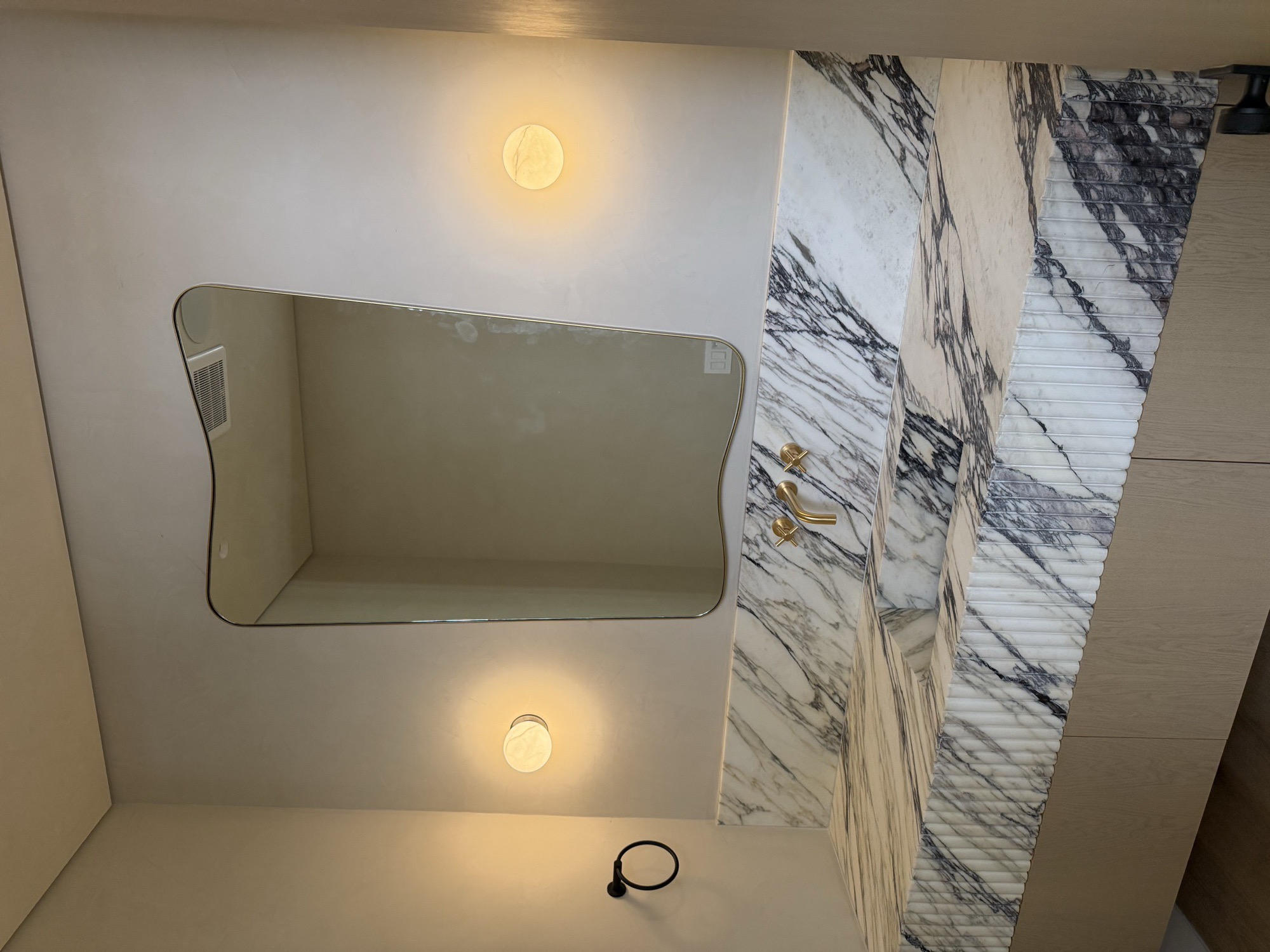 Organic gold-framed custom mirror above a marble vanity with brass wall-mounted faucet